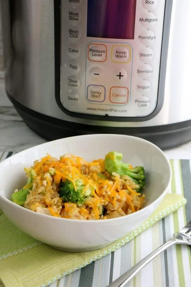 A close up of a bowl filled with cheesy chicken broccoli rice sitting in front of an Instant Pot