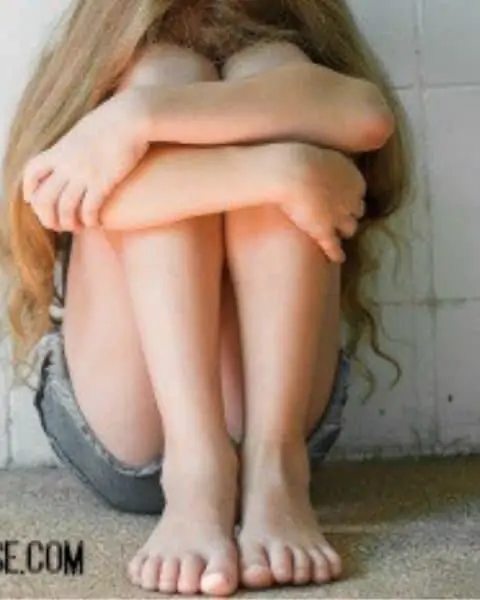 A young girl curled up and crying in her knees.