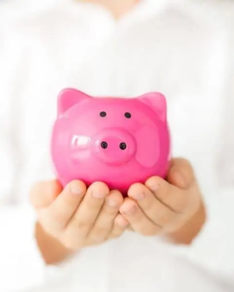 A small child holding a very bright pink piggy bank in her hands.