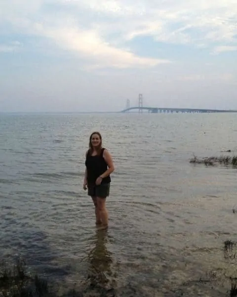 A woman standing in the water in front of Mackinac bridge.