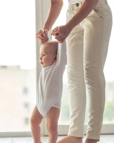 A parent helping her young child stand up on their own.