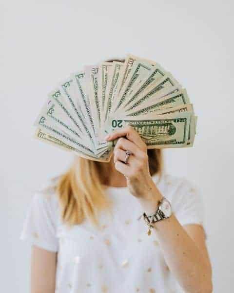 A woman with fanned out cash, including fives, tens, and twenty dollar bills.