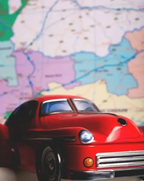 A red, classic car in front of a map.