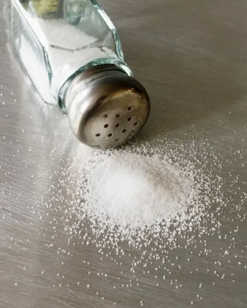 A salt shaker tipped over next to a pile of salt.