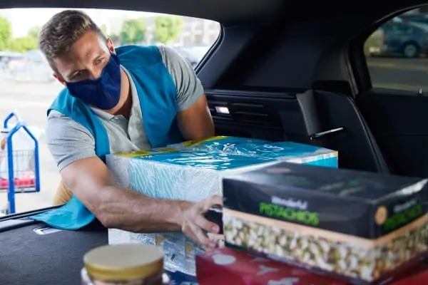 Man wearing face mask and loading groceries inside a vehicle. 