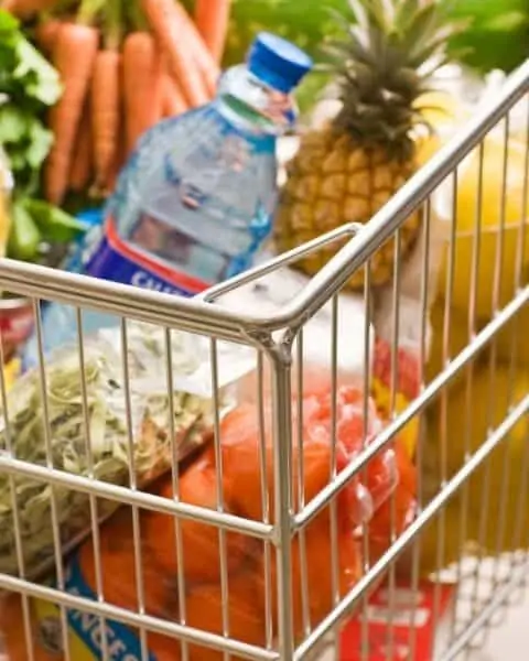 A grocery cart full of healthy produce including pineapple, asparagus, oranges, and carrots.