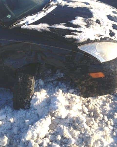 A car with the front tire turned sideways from the snow.