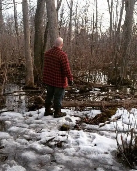 A man standing on snow and ice looking into the trees.