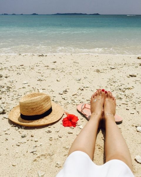 A woman sitting on the beach with her shoes off.