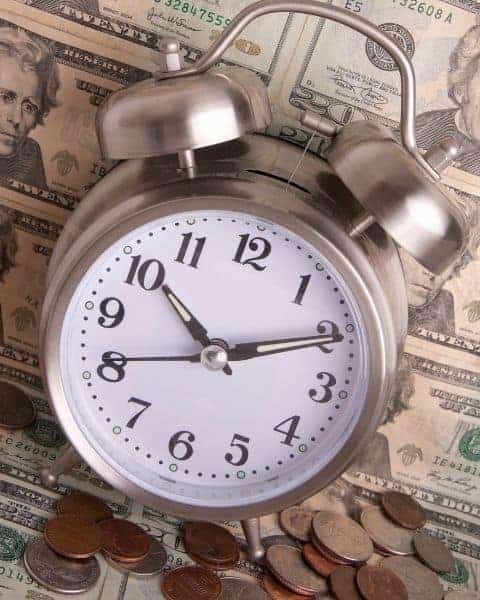 An alarm clock on top of $20 bills next to a stack of coins.