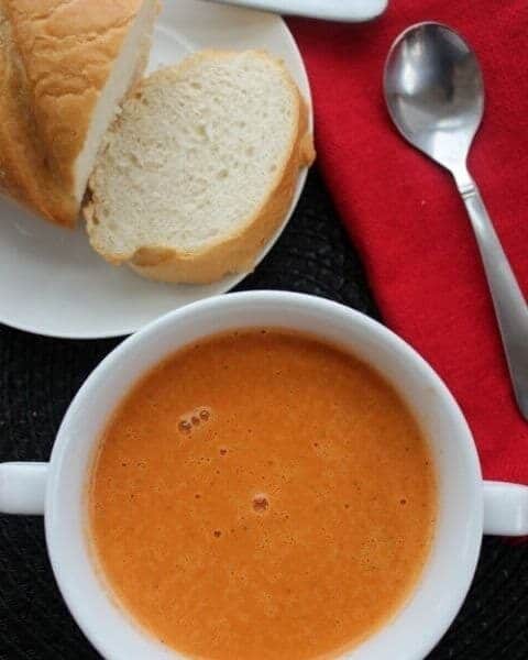 Creamy tomato soup with a loaf of bread next to the bowl.