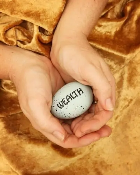 A woman holding an egg in her hands with the words "wealth" on the egg.