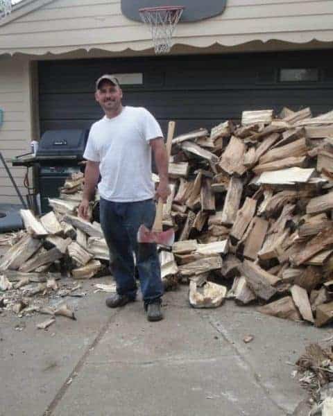 A man standing in front of a large pile of chopped firewood.