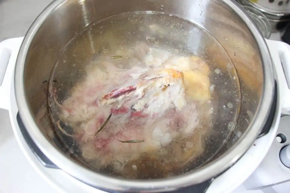 A chicken carcass inside of an Instant Pot covered with water and vinegar. 