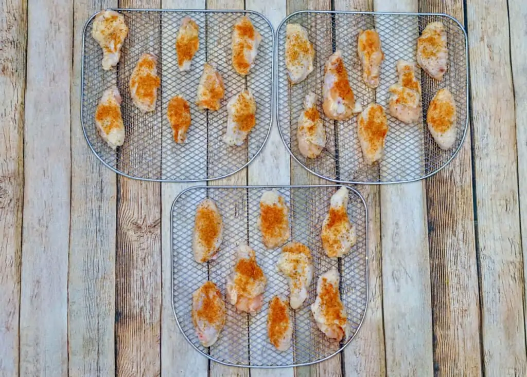 Seasoned chicken wings on three air fryer racks. 