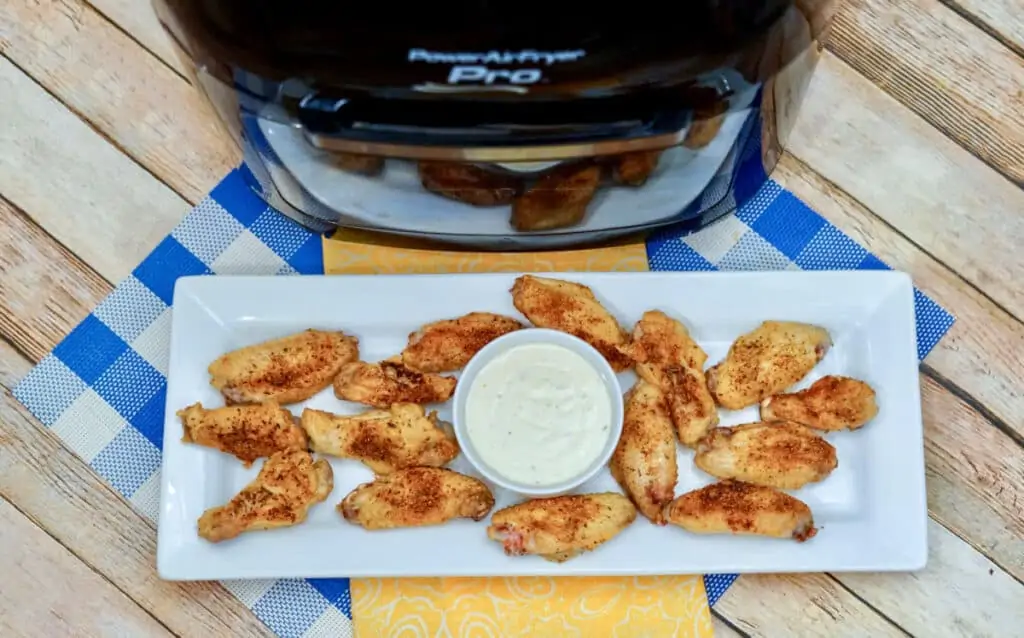 A plate full of cajun chicken wings with ranch dressing in a cup sitting in front of an Air Fryer.