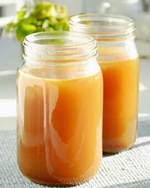 Two mason jars sitting on a countertop, filled with homemade bone broth. 