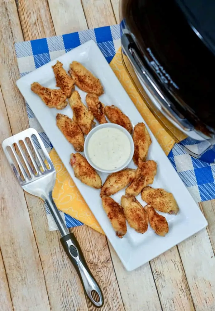 cooked chicken wings sitting on a plate with a cup of ranch dressing , next to an Air Fryer.