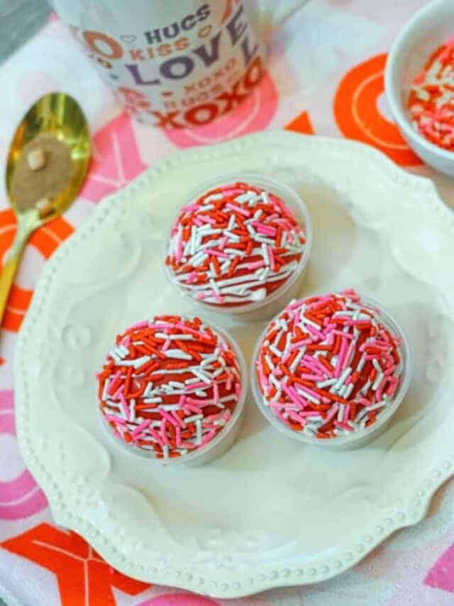 A white platter with three cups of different colors of sprinkles.