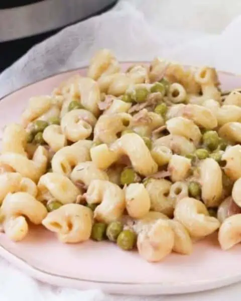 A white plate of tuna noodle casserole with green peas and sauce.