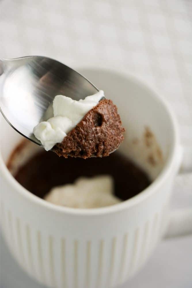 a close up photo of a spoonful of gooey chocolate mug cake with whipped cream. 