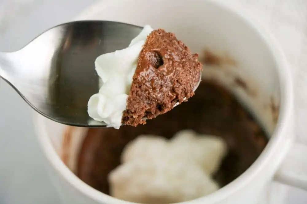 A close up of a spoonful of chocolate mug cake and whipped cream.