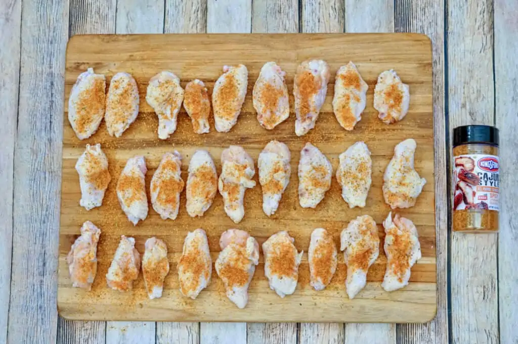 A bunch of raw chicken wings covered in Cajun seasoning blend on a wooden cutting board. 