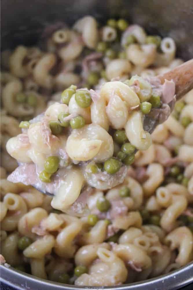Close up picture of a spoonful of creamy, cheesy tuna noodle casserole with peas.