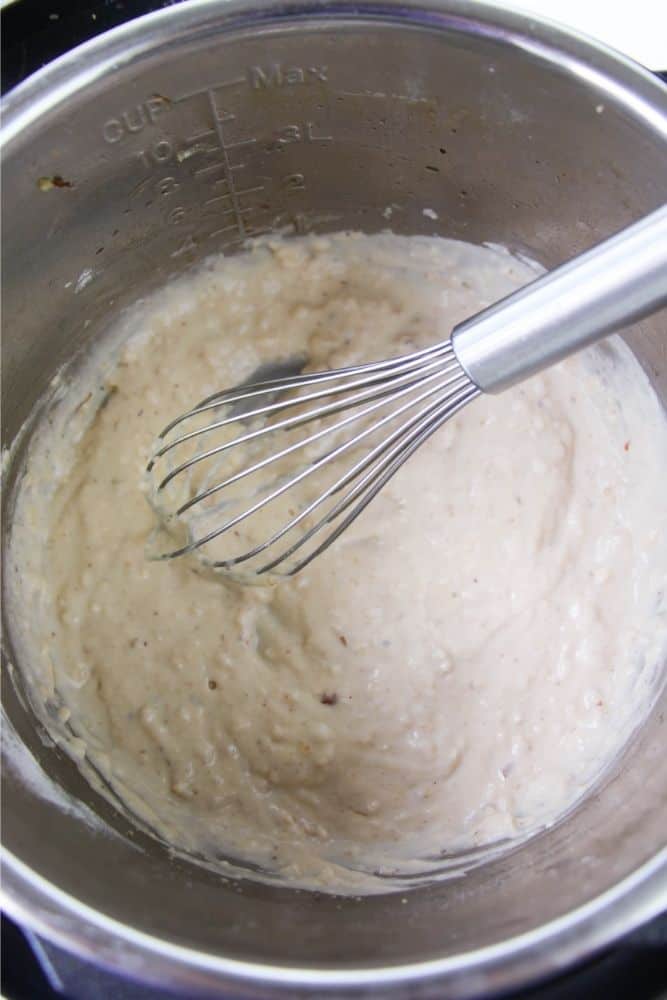 A whisk stirring a cream sauce inside an Instant Pot. 