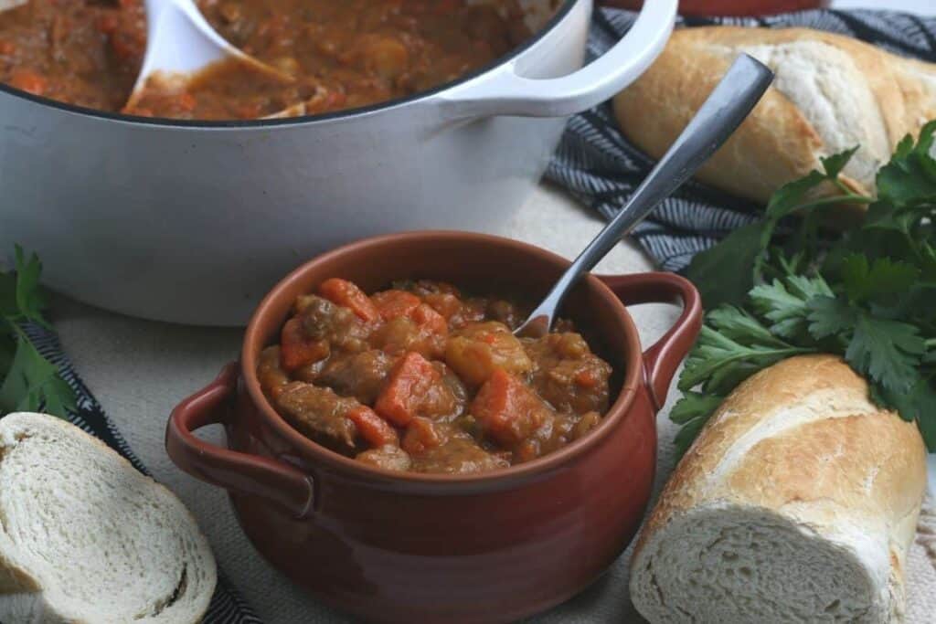 A bowl full of beef stew sitting on a table with bread. 