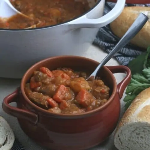 A bowl full of beef stew sitting on a table with bread.