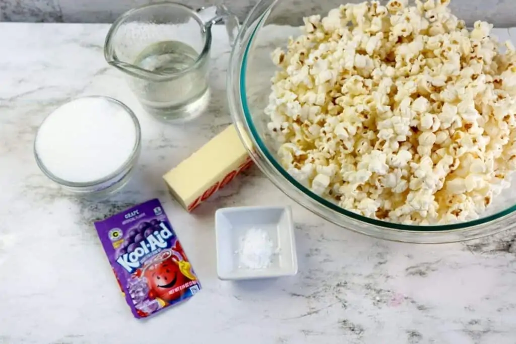 The ingredients for making flavored popcorn aitting on a table, including Kool-Aid drink mix, butter, corn syrup, baking, sugar and baking powder. 