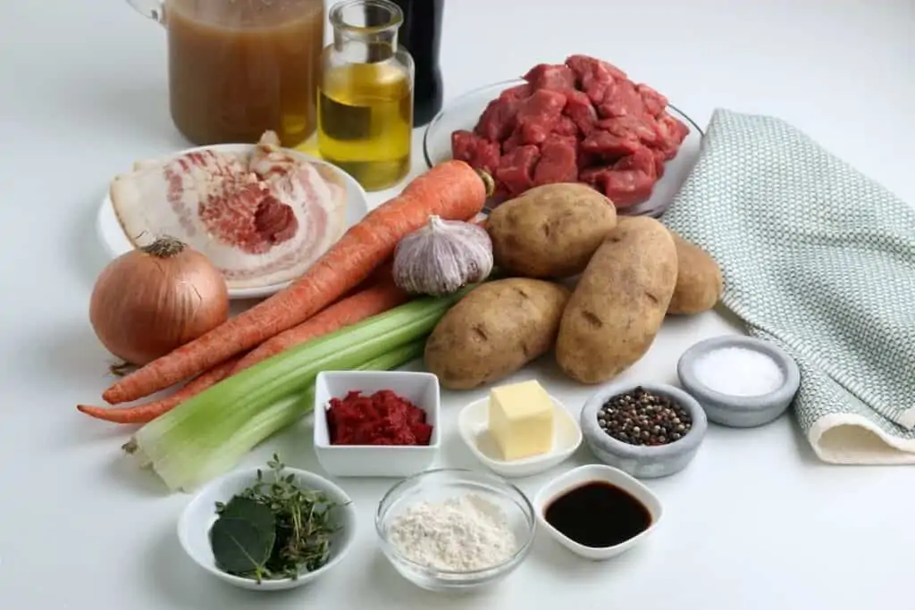 Irish stew ingredients sitting on a table including stew meat, potatoes, carrots, onions, celery and spices.