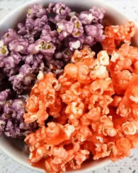 A bowl filled with purple and orange colored popcorn sitting next to several packets of Kool Aid drink mix.