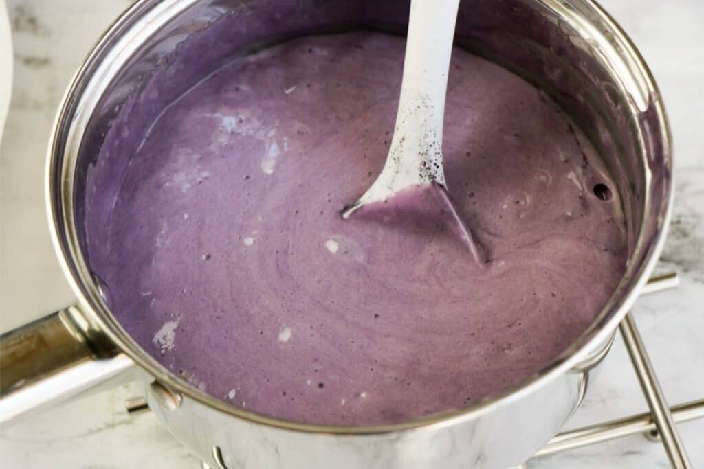 purple Kool-Aid flavored sugar sauce in a pot being stirred with a spatula.