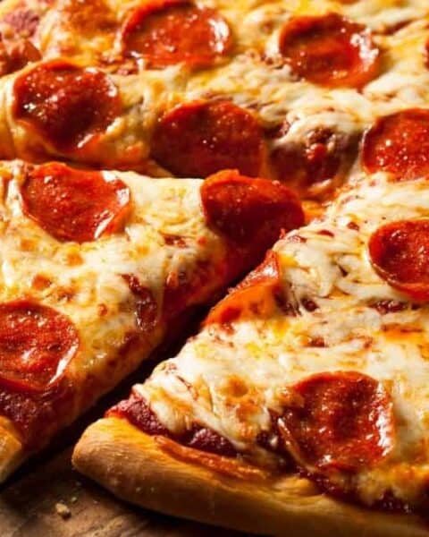 a slice of pizza being taken from a circle pepperoni pizza.