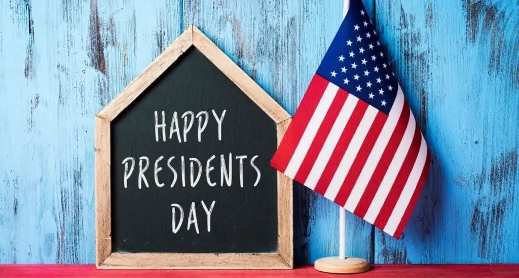 chalkboard sign that says Happy President's Day, sitting next to an American Flag on a table. 