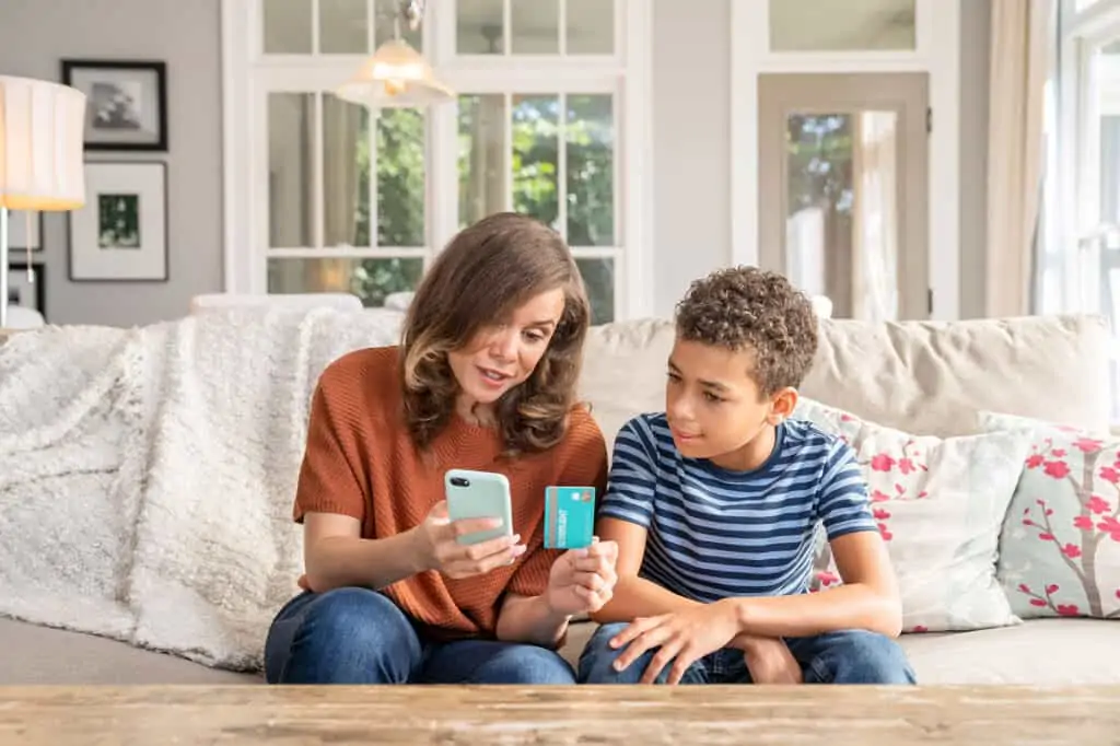 A mother and son sitting on the couch with a phone and credit card. They're discussing finances.