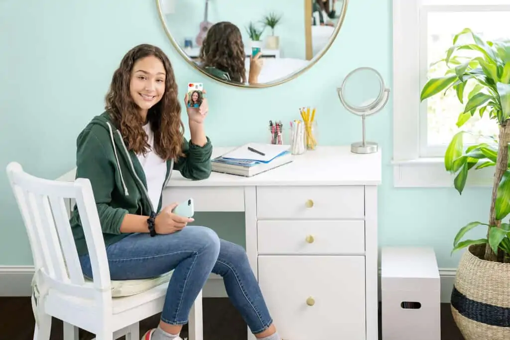 Teen sitting at her desk with a credit card showing the greenlight card.