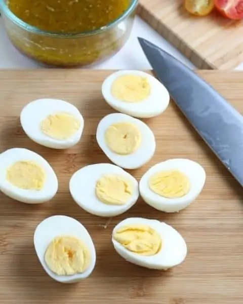 Hardboiled eggs cut in half on a cutting board with a knife.