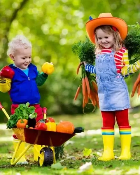 Two small children in boots and hats in the garden.