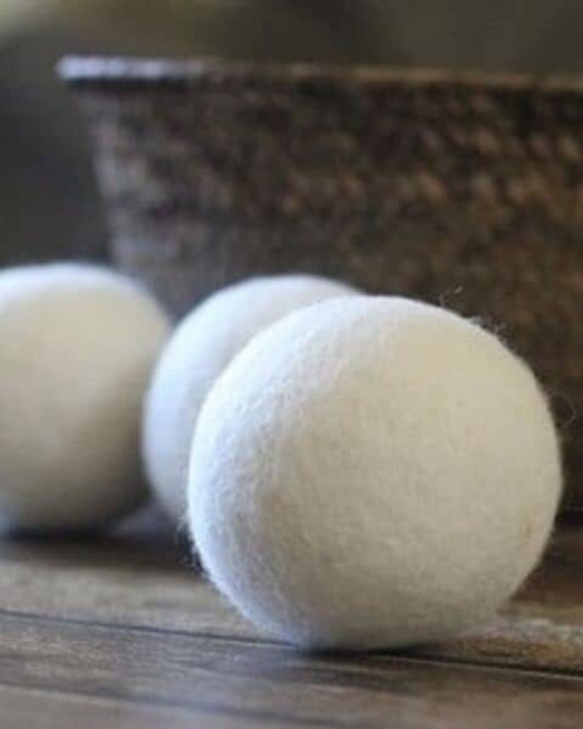 Three Wool Dryer Balls are placed on a wooden surface, with a textured brown basket in the background.
