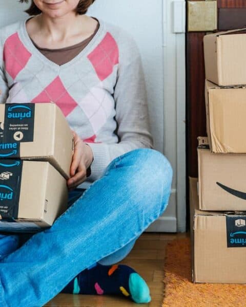 Stack of Amazon Prime packages delivered to a home door smiling woman begin to unbox the cardboard boxes.