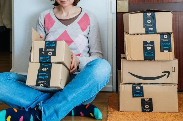 Stack of Amazon Prime packages delivered to a home door smiling woman begin to unbox the cardboard boxes.