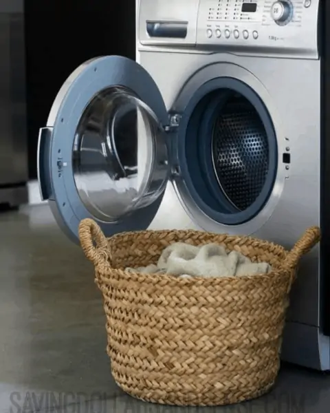 An opened washing machine with a basket full of clean sheets and clothes.