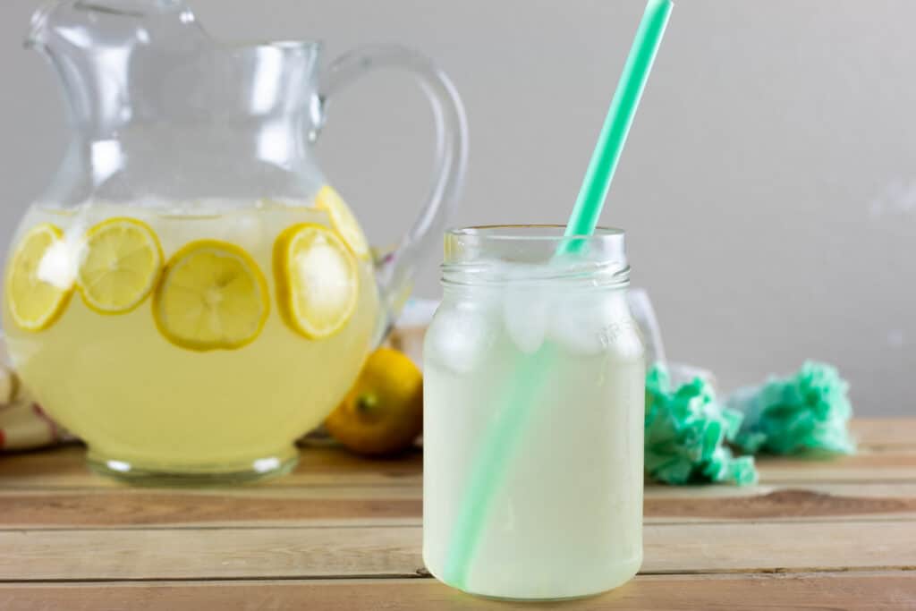 A jar of lemonade with a green straw sticking out.
