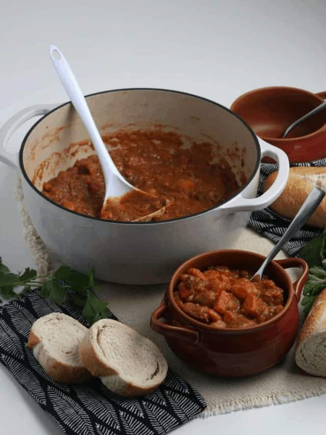 Beef stew in a pot next to slices of bread.