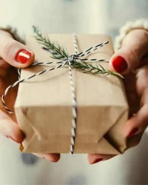 A woman holding a present that's wrapped in brown paper with beautiful ribbons.