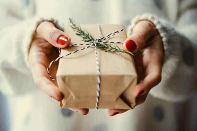 A woman holding a present that's wrapped in brown paper with beautiful ribbons.