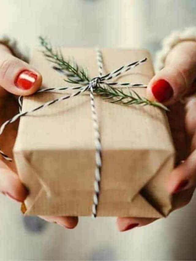 A woman holding a Christmas gift wrapped in brown paper with a green branch from a Christmas tree tied in string.